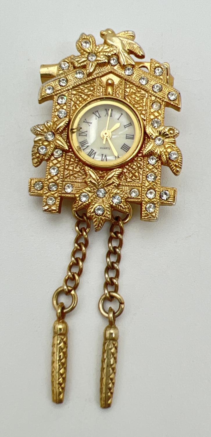 A gold tone Cuckoo clock pendant/brooch set with clear stones, by ETC Co. Ltd. Floral and bird