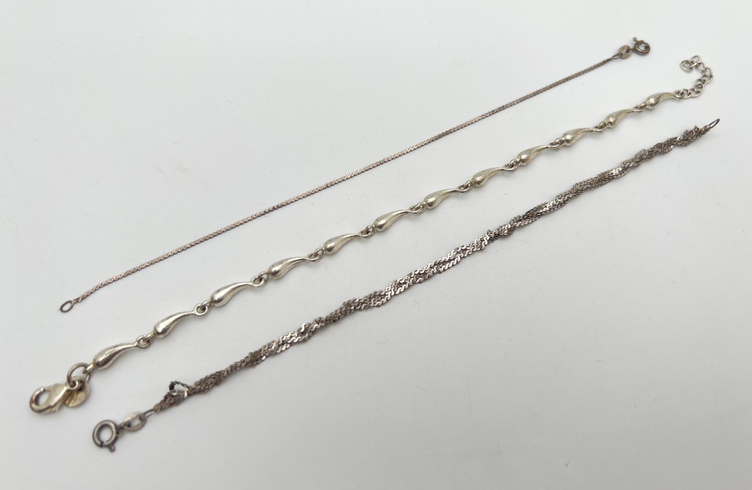 3 silver chain bracelets. A teardrop shaped link bracelet with lobster claw clasp; a plaited