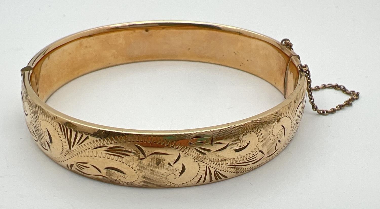 A vintage 9ct rolled gold bangle with half floral engraved pattern, push clasp and safety chain.