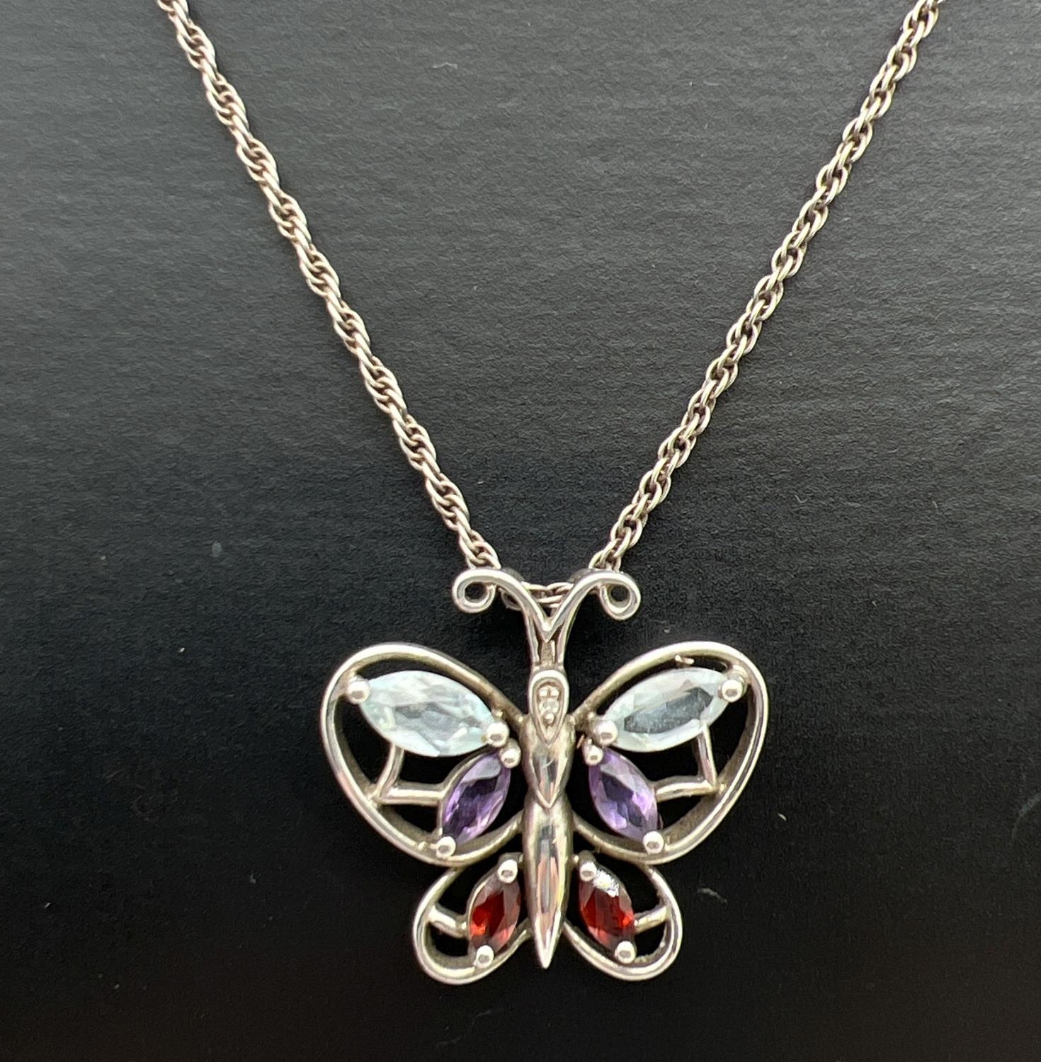 A silver butterfly pendant set with a diamond, amethyst, blue topaz and garnets. On an 18" rope