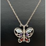 A silver butterfly pendant set with a diamond, amethyst, blue topaz and garnets. On an 18" rope