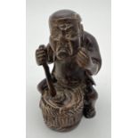 A carved wooden netsuke modelled as a man stirring a pot. Set with small mother of pearl disc to