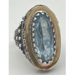 A silver modern design dress ring set with a large oval cut blue topaz stone. Rope design scroll