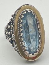 A silver modern design dress ring set with a large oval cut blue topaz stone. Rope design scroll