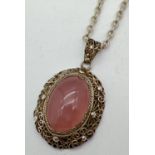 An oval shaped silver filigree style pendant set with a rose quartz cabochon, on an 18" belcher