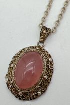 An oval shaped silver filigree style pendant set with a rose quartz cabochon, on an 18" belcher