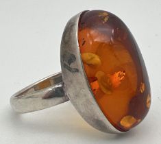 A large silver dress ring set with an oval cut amber cabochon. Ring size S. Silver mark to inside of