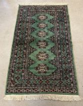 A vintage green ground rug with fringed ends, approx. 176cm x 93cm.