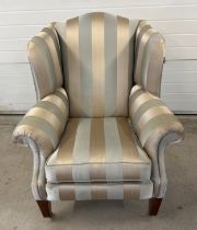 A modern Duresta wing back arm chair with brass caster front feet and gold striped upholstery.