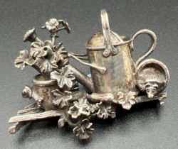 A boxed silver brooch in the shape of a watering can with geraniums, flowers pots and a hedgehog, by