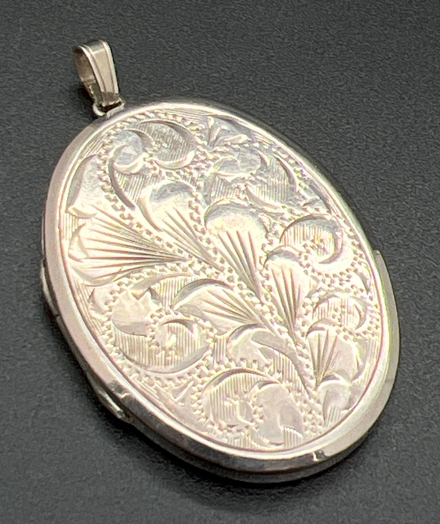A large vintage silver oval shaped locket with floral engraving to front and engine turned