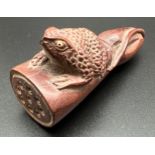 A carved wooden Japanese netsuke of a frog sat on a log. Set with signed small ivory disc to