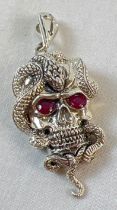 An unmarked white metal pendant in the form of a skull with a snake, set with rubies for eyes.