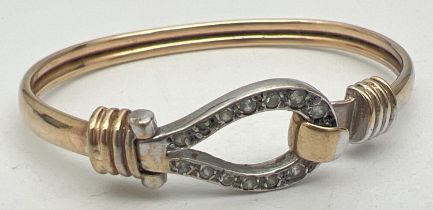 A yellow and white 9ct gold child's bangle with clear stone set hook and eye clasp. Gold marks to