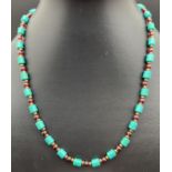 An 18" Chinese turquoise and garnet beaded necklace with gold tone T bar clasp with floral detail.