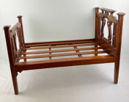 An Edwardian wooden dolls bed with slatted base, tapered legs and shaped bed ends, stepped finals to