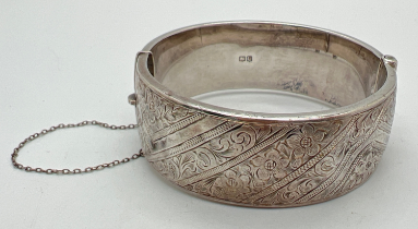 A vintage silver bangle with half floral engraved detail and safety chain (a/f). Full hallmarks to