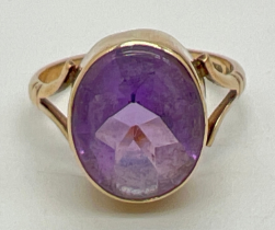 A 9ct gold and amethyst set dress ring. A large oval cut bezel set amethyst with shaped shoulders to