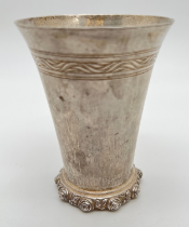 An Omar Ramsden Arts & Crafts silver beaker of hammered conical form with rose design rim to base.