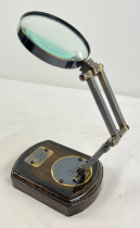 A desktop magnifying glass on a hinged folding stand with plaque for Watkins & Hill, on wooden base.