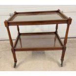 A vintage dark wood tea trolley with turned legs and glass inserts to shelves.