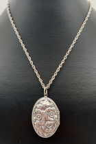 A large oval silver locket with floral design in relief to front. On a 20" rope style chain with