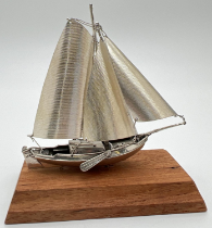 A vintage silver model of a sailing boat mounted on a wooden plinth. Very well detailed with matte