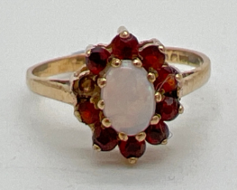 A 9ct gold opal and garnet dress ring. Central oval cut opal surrounded by garnets (1 missing).