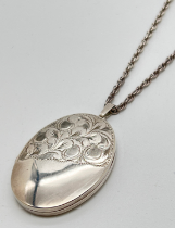 A large vintage silver oval shaped locket with half engraved detail of scroll & foliate design. On a