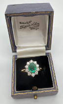 A 18ct gold emerald and diamond cluster ring. A central oval cut emerald surrounded by 10 round