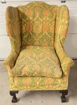 An antique dark wood wing back chair with ball and claw carved front feet and green, yellow and