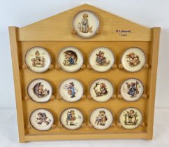 A collection of 13 assorted M.J. Hummel Goebel ceramic miniature plates together with a wooden