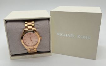 A boxed ladies wristwatch by Michael Kors. Gold tone stainless steel strap and case with pale rose