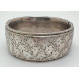 A vintage silver bangle with push clasp and half floral engraved decoration. Silver marks to