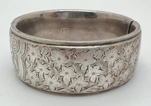 A vintage silver bangle with push clasp and half floral engraved decoration. Silver marks to