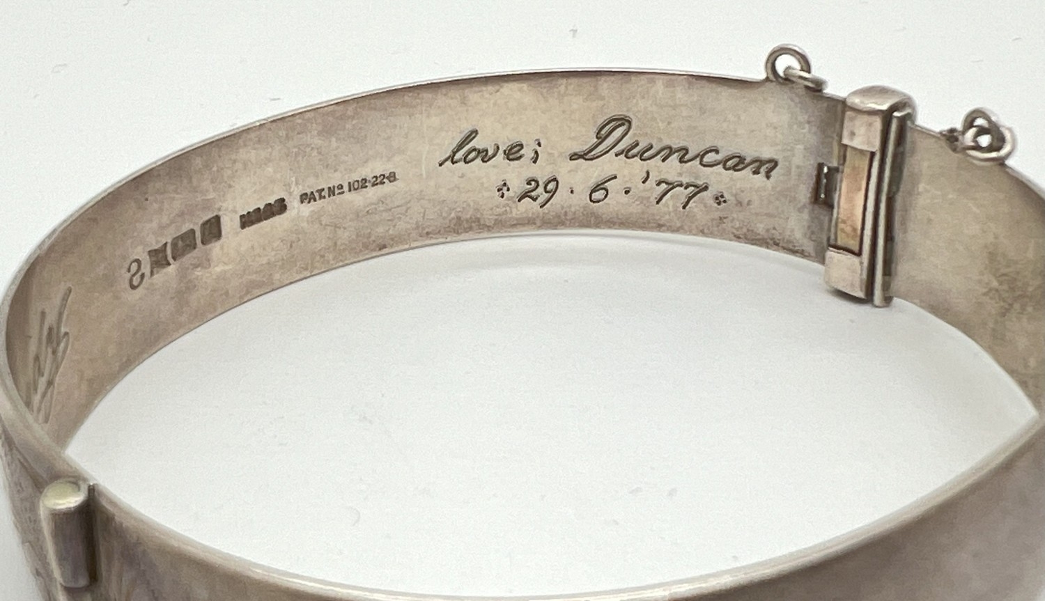 A vintage silver bangle with half floral decoration, push clasp, safety chain and inscription to - Image 2 of 2
