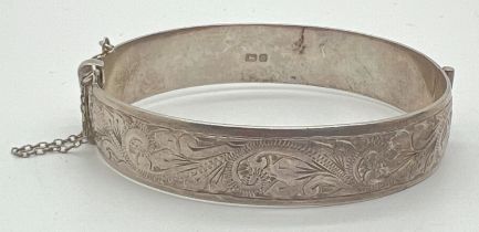 A vintage silver bangle with half floral decoration, push clasp, safety chain and inscription to