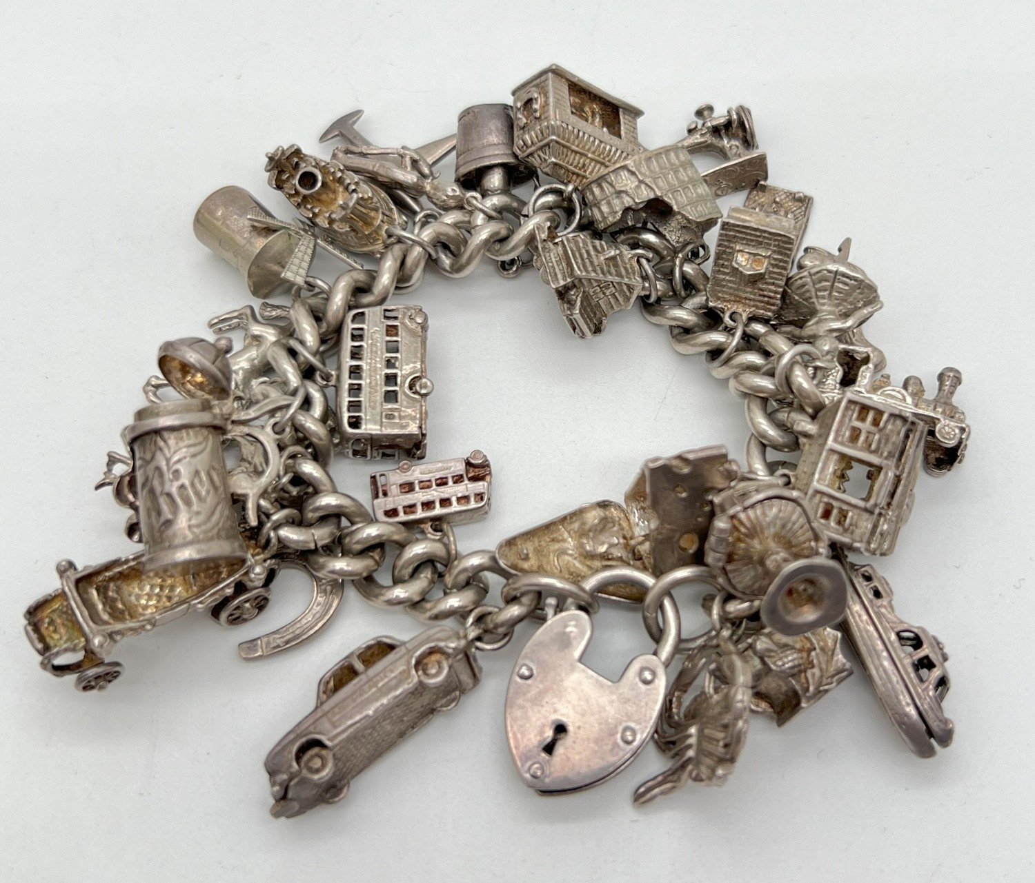 A vintage silver charm bracelet with large padlock clasp and 29 silver and white charms - some
