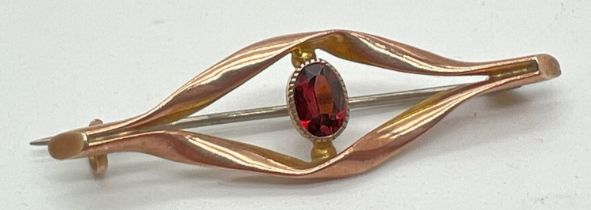 A 9ct gold brooch of twist design set with central oval cut garnet stone. Marked '9ct' to reverse.