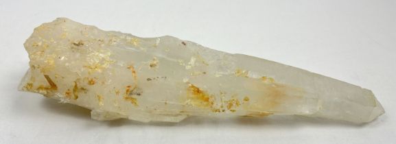 A large clear quartz natural laser wand with orange, brown and black inclusions. Areas of small