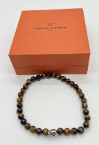 A boxed Simon Carter, London, men's tigers eye bead and silver tone skull bead expanding bracelet.