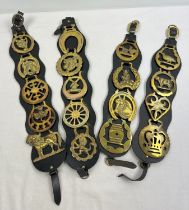 4 black leather hanging straps with horse brasses in varying sizes and designs. To include