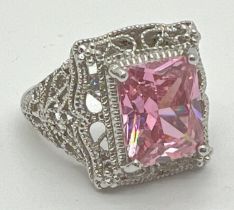 A large silver cocktail ring with decorative filigree style mount, set with a large pale pink square