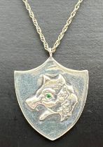 A modern silver shield shaped pendant necklace designed with a wolfs head and set with a small green