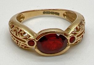 A 9ct gold garnet set dress ring with openwork scroll decoration to both shoulders. Central bezel