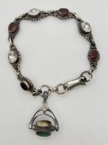 A white metal bracelet set with alternating oval cut garnets and clear quartz with a rotating fob