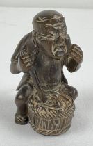 A small carved wood netsuke of an Oriental man stirring a barrel. Set with small mother of pearl