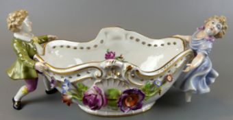 Ovale Schale, gehalten von 2 Porzellanfiguren, außen plastische Blumen,