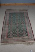 Afghanistan style wool rug with a green white and red ground, decorated with diamond lozenge guls