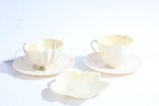 Two Belleek cabinet cups and saucers, the cups with shell pattern bowls, one raised on three shell